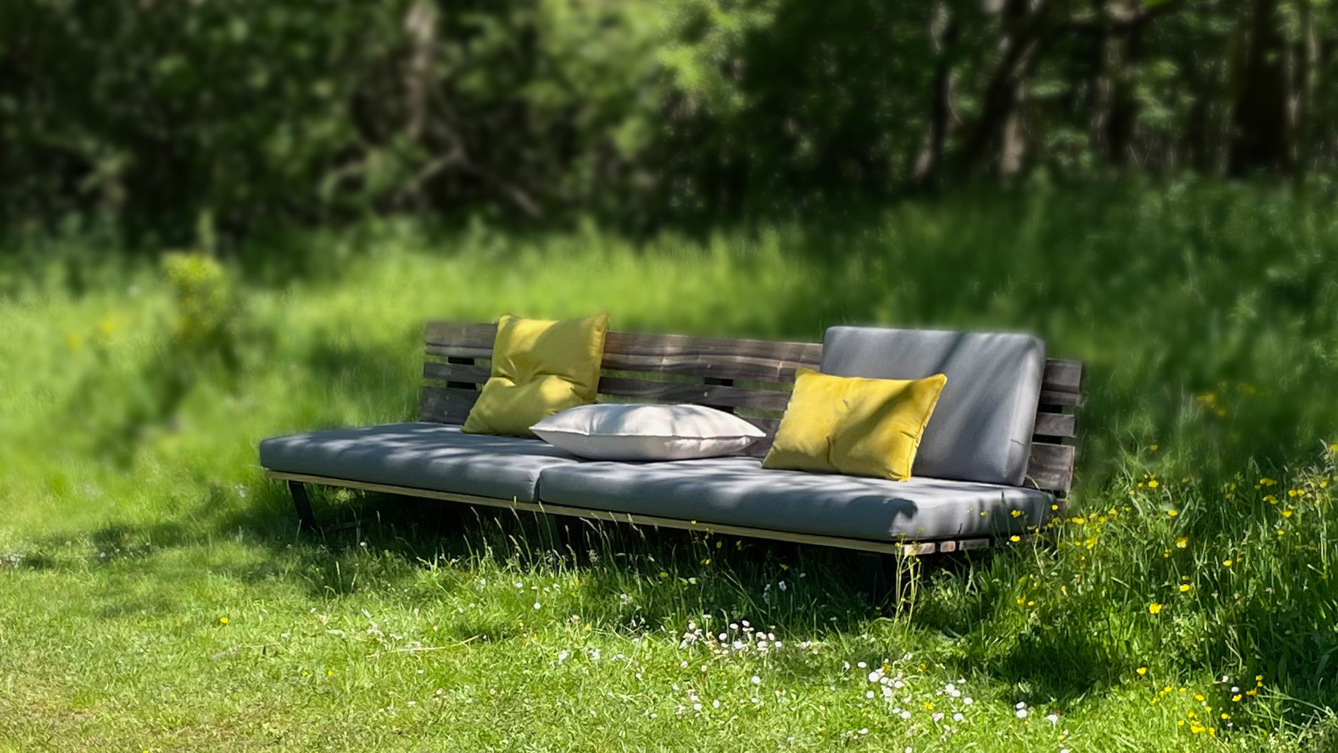 Loungebank met grijzen en gele kussen in grasveld